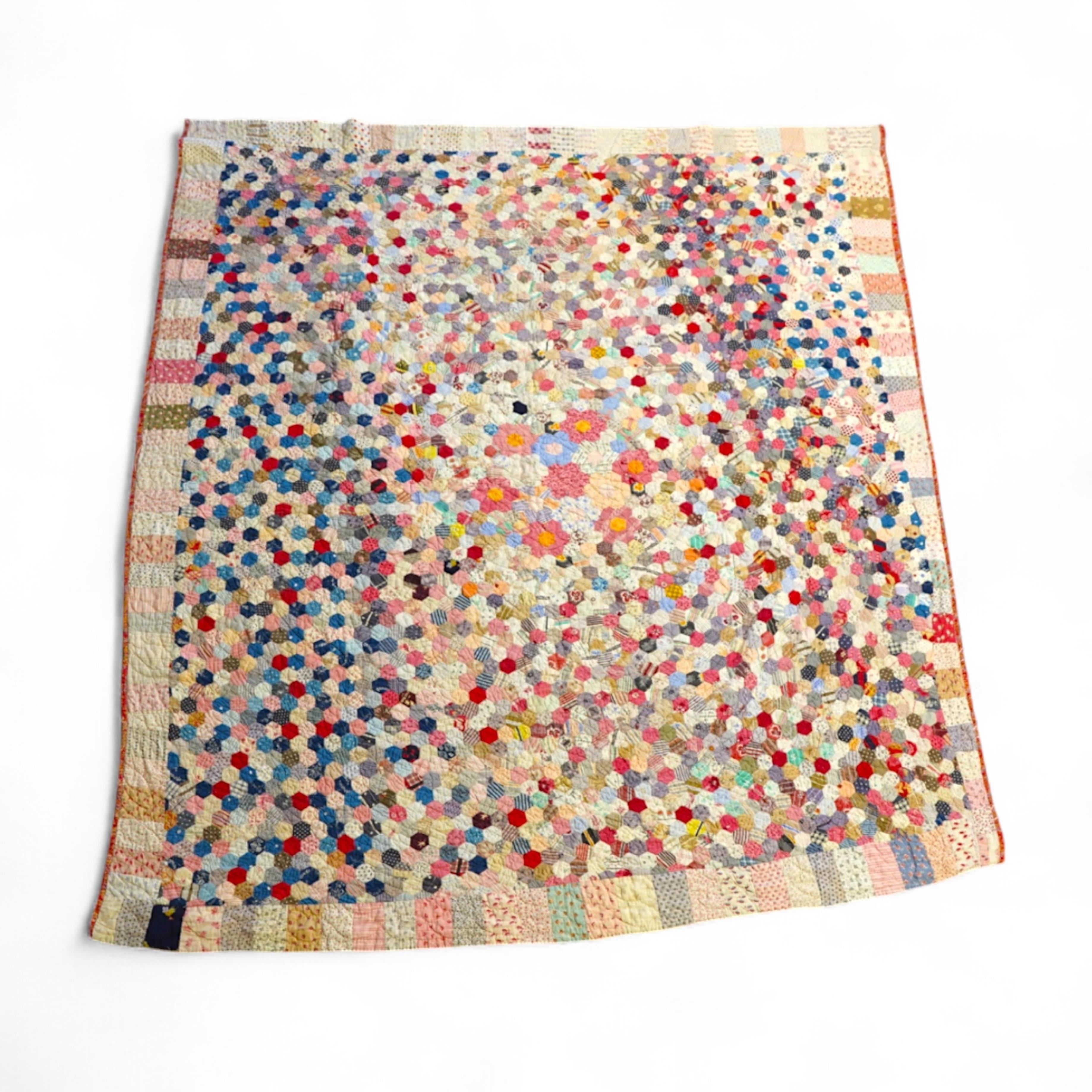 An English cotton hexagon hand made and hand pieced quilt, made from a large variety of printed dress fabrics from 19th century. The quilt edged with a wide stripped multi fabric border. The under side designed in wide s